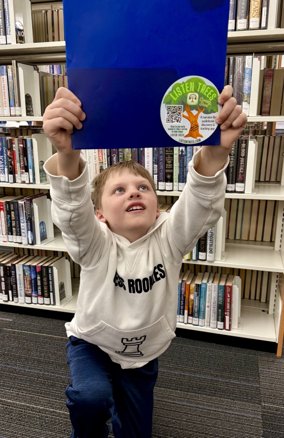 One of the boys holding up a folder with a Listen Trees sticker at the library